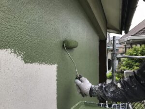 グリーン系塗料をローラーで外壁に塗装しているイメージ